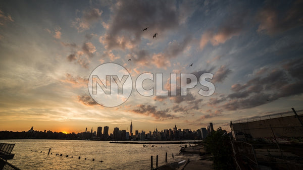 Manhattan skyline silhouette with birds flying in beautiful orange sunset sky in early evening over East River water in NYC