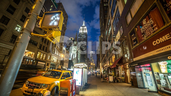 Lower 5th Ave at night with Empire State Building and walk light and parked caravan taxi cab