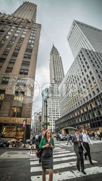 Chrysler Building towering over Midtown Manhattan - woman on smartphone crossing street on cloudy summer or spring day