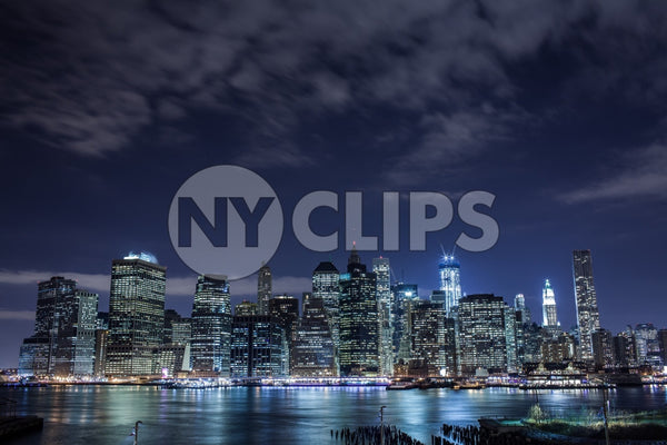 Manhattan skyline with incomplete Freedom Tower at night - clouds overhead across East River water in HDR