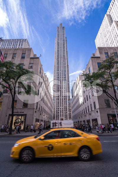 taxicab driving past Rockefeller Center on beautiful bright sunny day with blue sky and clouds in Midtown Manhattan