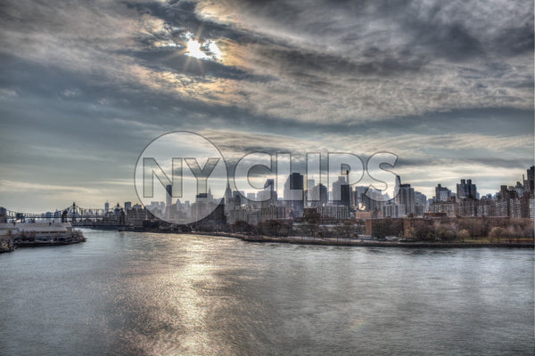 Manhattan skyline from across East River in late afternoon early evening - sun beaming through clouds onto water in HDR