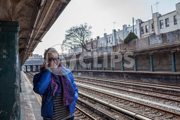 woman on cell phone - outdoor subway platform in winter - elevated train station tracks