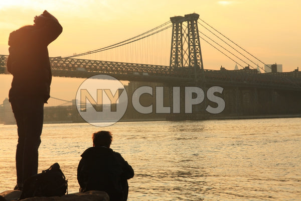 Manhattan Bridge at sunset - people enjoying view of beautiful orange sky over East River from Brooklyn