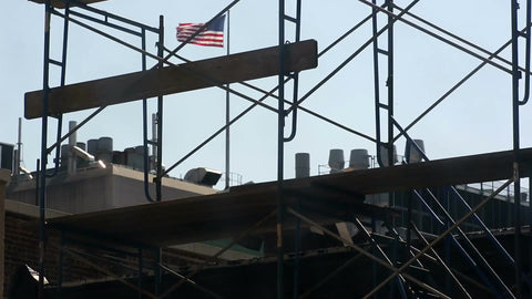 construction scaffolding with American flag on building rooftop waving in background in NYC