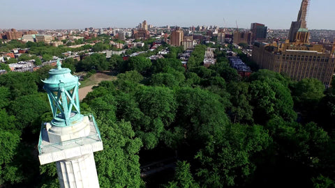 aerial of Prison Ships Martyrs' monument - circling Fort Greene Park in Brooklyn with trees and Manhattan skyline with buildings and skyscrapers in background