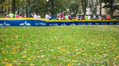far shot of leaves on ground - green grass and trees with Marathon runners in background in Central Park in spring 1080 HD in NYC