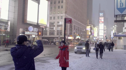 Asian man taking picture of tourist woman in winter in Times Square - snowing in 4K and 1080 HD in NYC