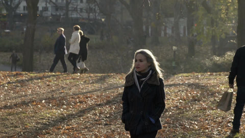 woman in autumn walking through Central Park on cold fall winter day with trees and leaves on ground, slow motion