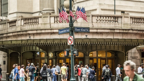 American flags on corner of East 42nd st outside Grand Central Station Terminal in Midtown Manhattan - people on crowded street on summer day