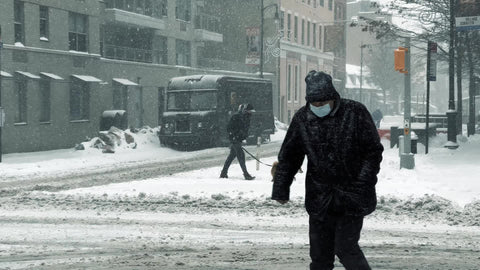 man in medical mask walking in snow in winter blizzard - snowing in NYC