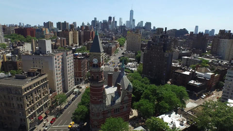 aerial of Jefferson Market Library clock tower in Greenwich Village backing up with Manhattan skyline skyscrapers in background in NYC