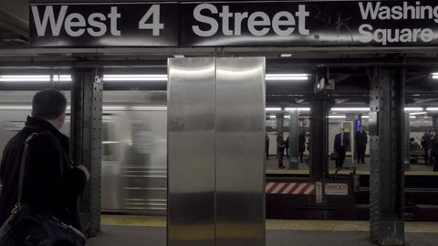 West 4th Street sign in subway station with train passing on platform in NYC