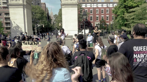 Black woman giving speech at BLM rally with diverse audience in Washington Square Park New York City