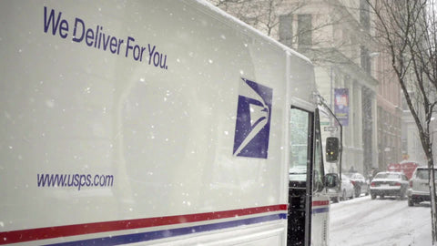 snowing on USPS we deliver for you slogan on mail delivery truck parked on street winter blizzard NYC