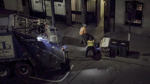 sanitation workers throwing trash bags into garbage truck at night in winter NYC
