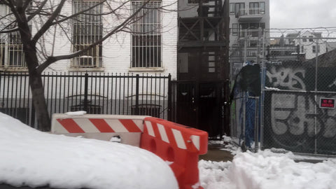 driving past gritty graffiti on fence and borded up building in winter with snow in Brooklyn New York City NYC