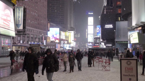 ads and red picnic tables in middle of Times Square, snowing in cold winter, people with coats and hats