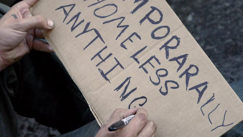 close-up of temporarily homeless anything helps sign - man writing on cardboard with marker