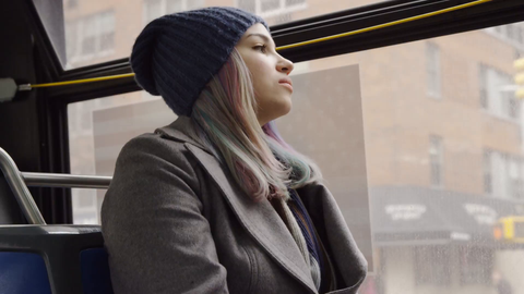 pretty woman in hat and coat riding bus looking out window in winter through city in 4K - slow motion on gloomy cold day in NYC