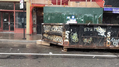 gritty garbage dumpster with graffiti snowing on street New York City NYC