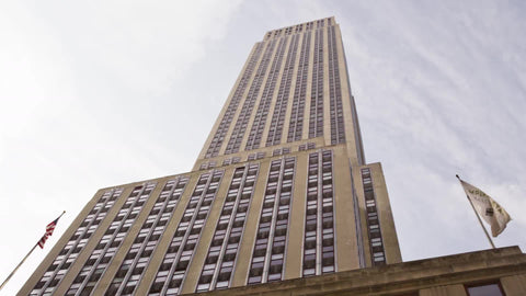 towering upward angle driving shot of Empire State Building front with American flag on 5th ave in Manhattan