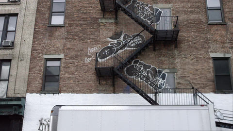 truck driving by graffiti on building with fire escape in gritty urban area