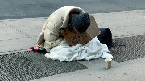homeless man with sign and cup sitting on sidewalk in New York City