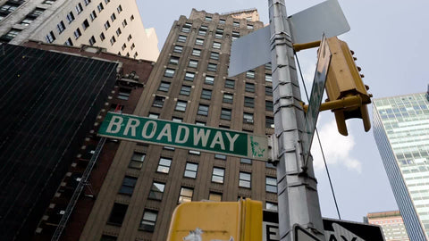 Broadway sign - one way arrow and intersection in Midtown Manhattan with tall skyscraper on summer day