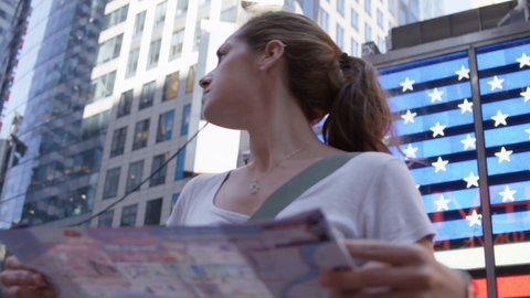 close-up of attractive female tourist looking at map in front of Times Square American flag LED - slow motion 4K in New York City