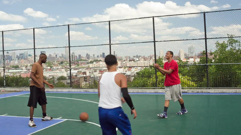 kids playing pickup basketball game on summer day with view of Manhattan skyline from fence