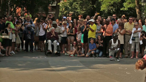 street performer acrobat jumping and flipping over row of volunteers - people clapping for show in Washington Square Park on summer day in NYC