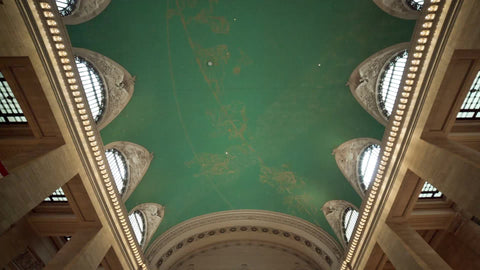 tilting down from Grand Central Station terminal ceiling to information desk with clock and people waiting in NYC
