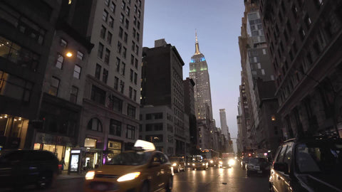 Empire State Building with colorful lights and cars in Manhattan traffic, headlights on street in early evening on Lower 5th Ave in 4K and 1080 HD in NYC