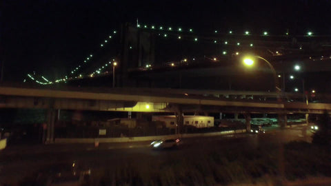 aerial of cars driving on FDR Drive and Brooklyn Bridge at night