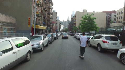 aerial of kid skating down Chinatown street rising to view of Manhattan skyscrapers