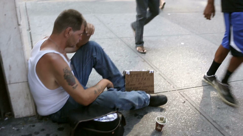 woman giving food to homeless veteran sitting on sidewalk with sign and cup in Manhattan New York City