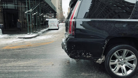 black Cadillac Escalade SUV driving through snow rain ice sleet and slush in cold winter Manhattan New York City NYC