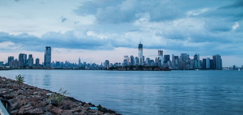 Downtown Manhattan skyline with skyscrapers and East River water view from Brooklyn with rocks in foreground in early evening