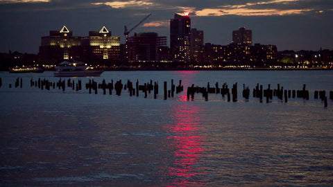 New Jersey skyline buildings and the W Hotel across Hudson River at night with wood dowels in water from Manhattan NYC