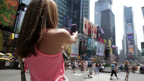 woman with sunglasses taking selfie in middle of Times Square on bright sunny day in summer