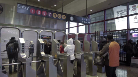 turnstiles in Times Square subway station at night, people entering and exiting in winter
