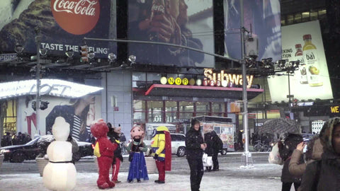 performers in Disney costumes - snowman in Times Square, snowing at night with bright lights on subway station sign - NYC