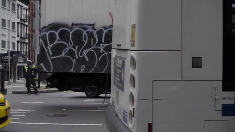 graffiti on truck and taxi cab driving in traffic with tram and Queensboro Bridge in background during day on east side of Manhattan in NYC