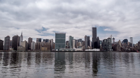 slowly zooming out from Manhattan skyline across East River water - reflection of Empire State Building and UN skyscrapers - 4K in NYC