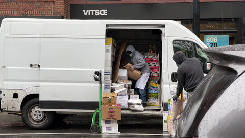 two men unloading supplies from van for restaurant in rain in winter in New York City NYC