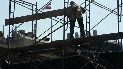 construction worker laying down wood plank on scaffolding - man in hardhat with American flag on roof in NYC