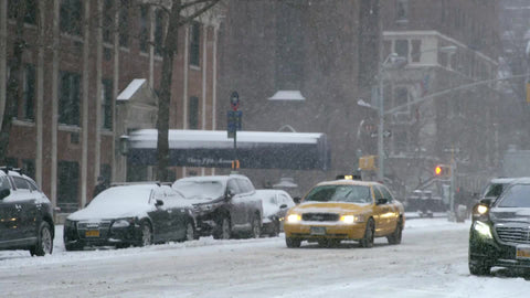 taxi cab and cars driving and man man walking bundled up in coat and hat in winter blizzard - snowing on 5th Ave in slow motion - snow in Manhattan New York City, NYC 4K and 1080 HD