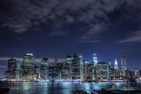 Manhattan skyline with incomplete Freedom Tower at night - clouds overhead across East River water in HDR