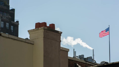 American flag waving on building rooftop with steam, steaming pipe chimney in Manhattan
